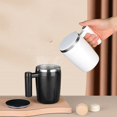 Le Monde Tech black blender with handle alongside white vitamix blending cup in hand on wooden surface